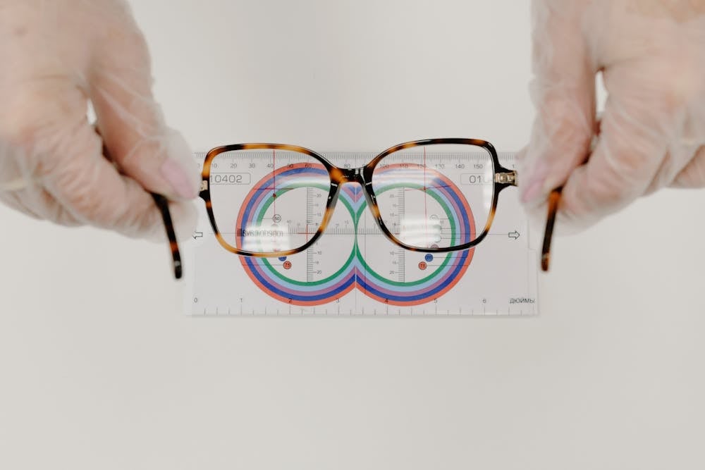 Gloved hands holding a pair of tortoiseshell eyeglasses over a lens measuring chart.